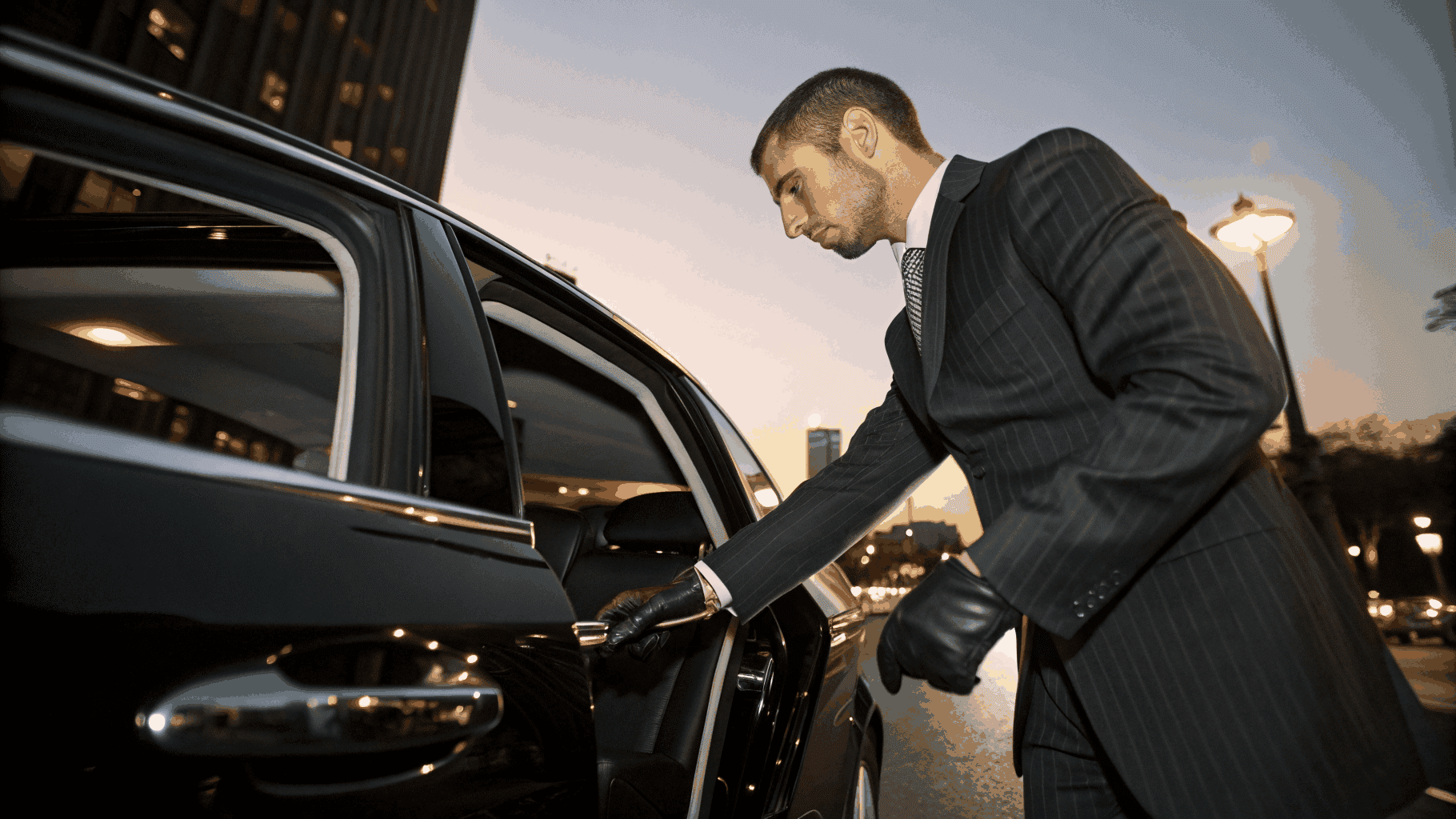 Professional chauffeur in black suit holding open rear door of Santa Limo branded luxury sedan at airport terminal